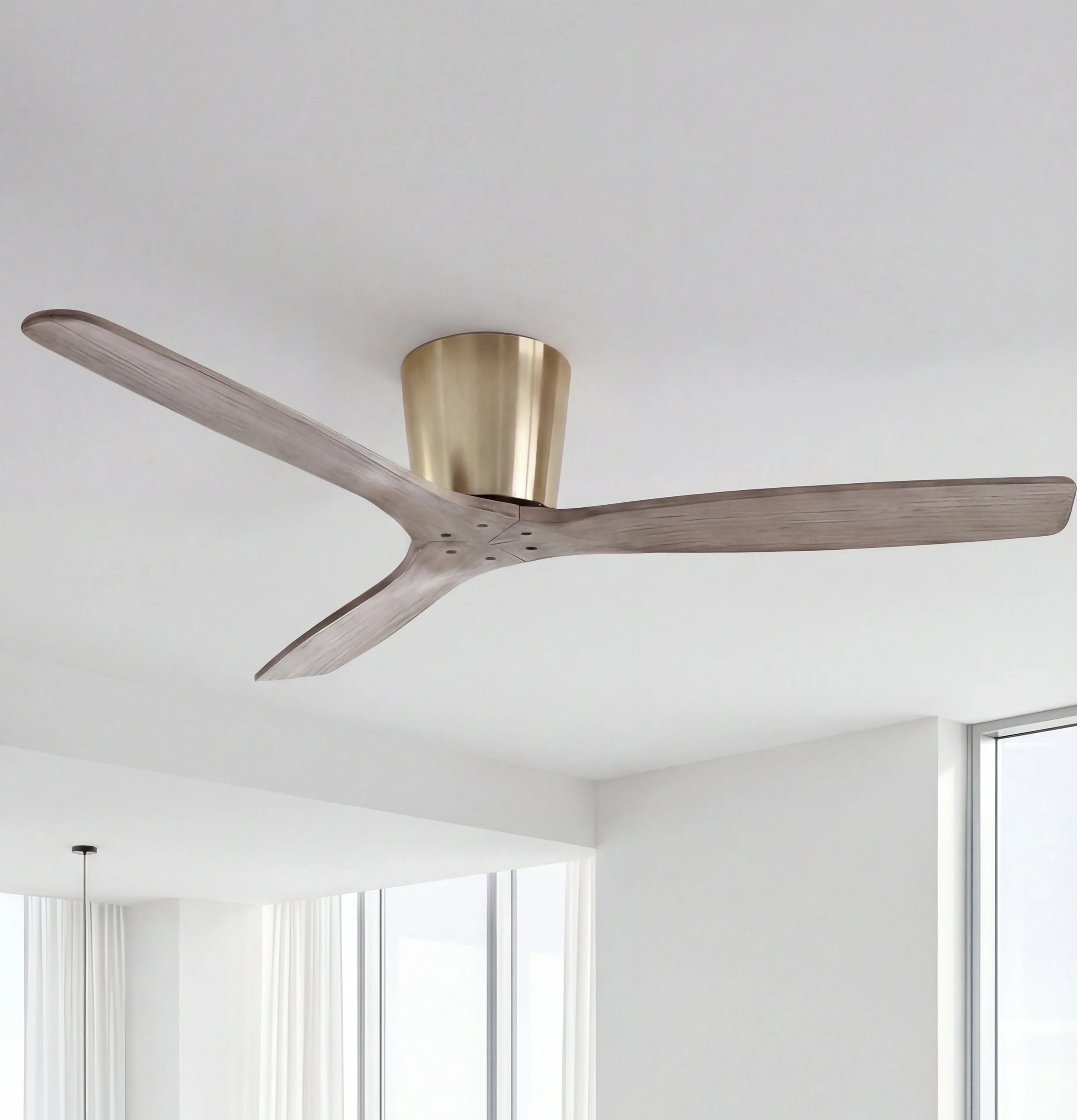 Modern ceiling fan with wooden blades and brushed gold mount in a bright, minimalist room