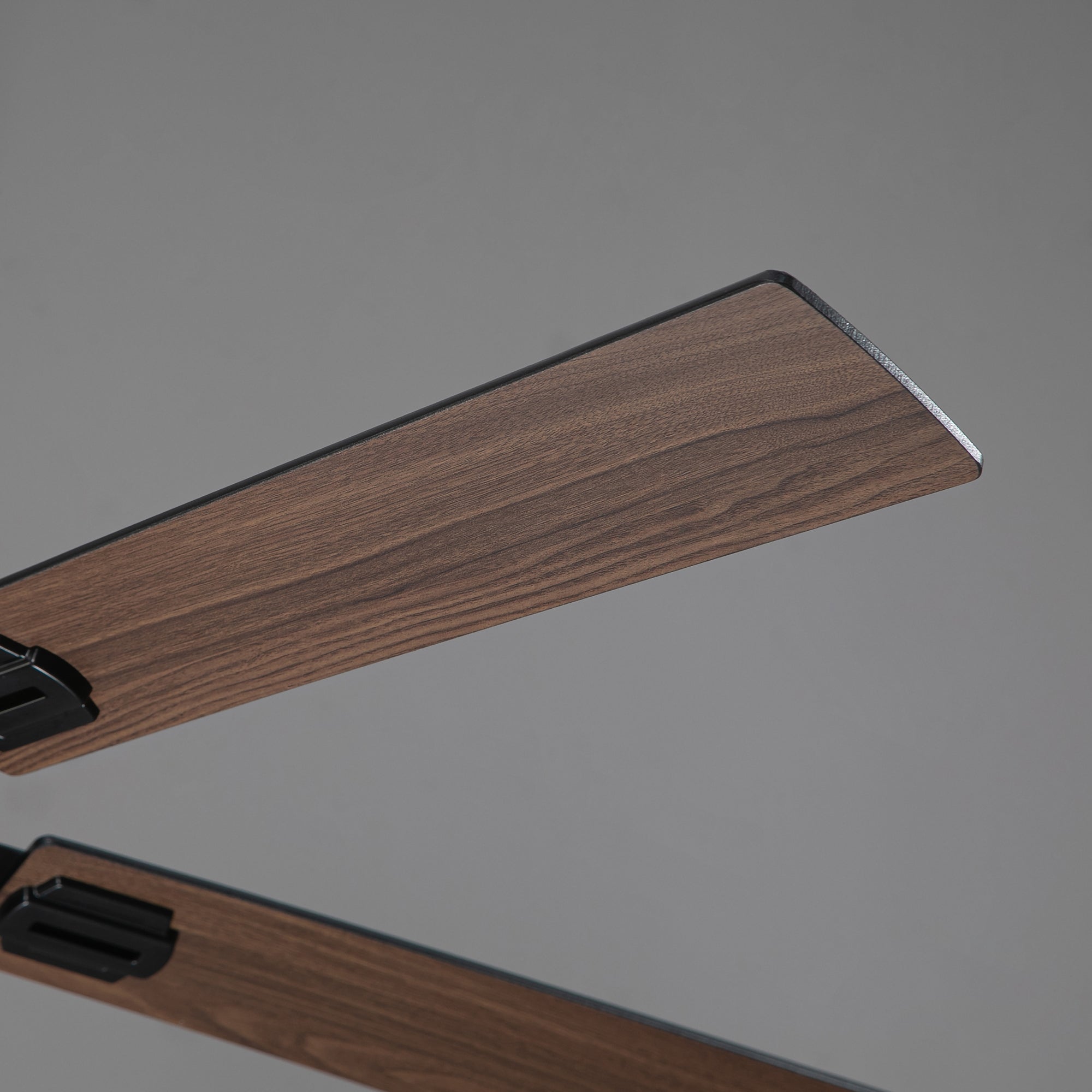 Close-up of modern ceiling fan blades with a wood finish against a gray background